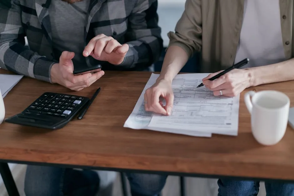 Two people reviewing paperwork and using a calculator to compute taxes, illustrative stock photo.